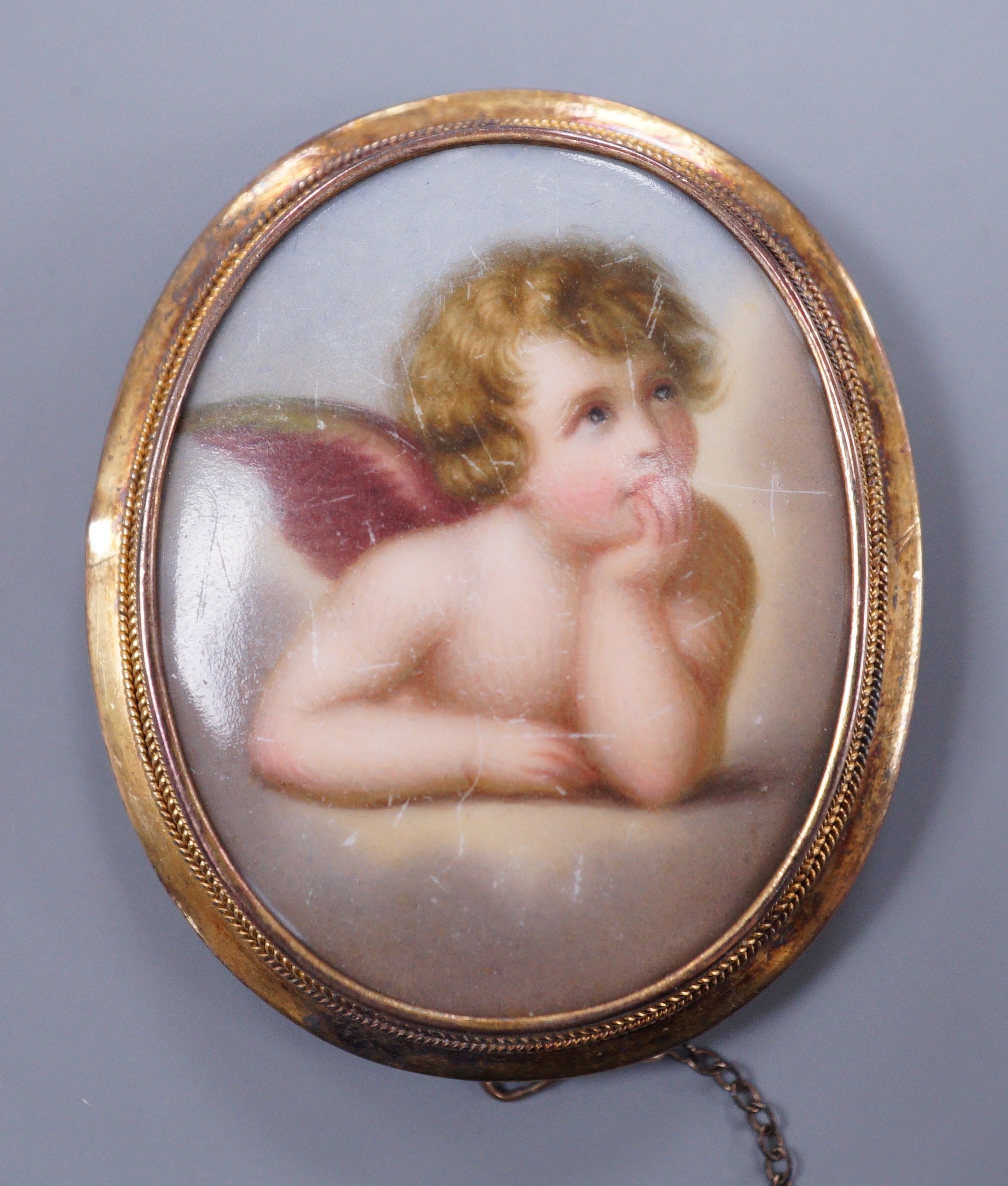 A Victorian gold mounted porcelain brooch decorated with Cupid, 5cm